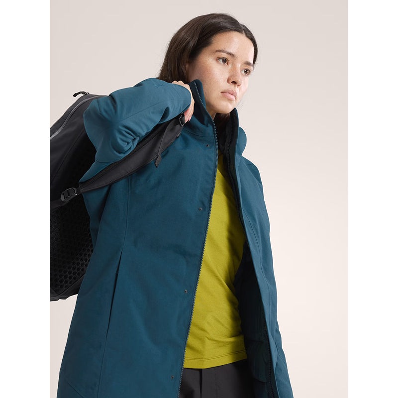 Person wearing a blue jacket holding a black backpack against a neutral background