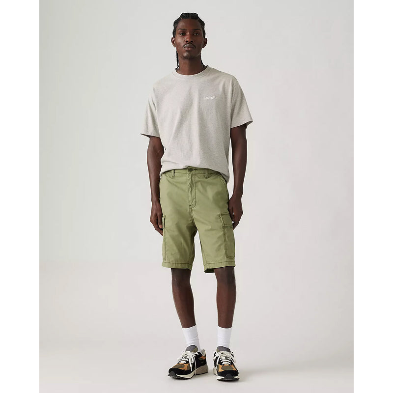 A man standing in a relaxed pose wearing black Carrier Cargo shorts and a grey t-shirt, with reflective details on the cuffs and a utility pocket design.