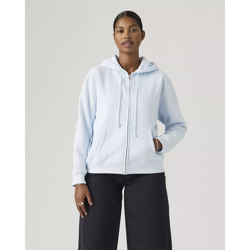 Woman wearing a light blue hoodie and black pants on a plain background