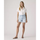 Woman wearing a white shirt and light blue denim shorts on a plain background