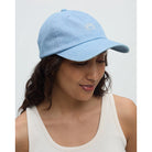 Woman wearing a light blue cap with a logo on a plain background
